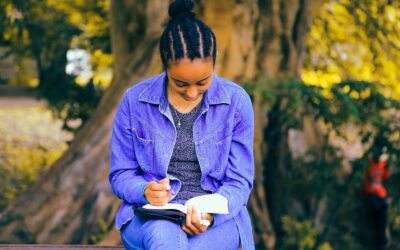A woman sits underneath a tree reading a journal about autism and eating disorders.