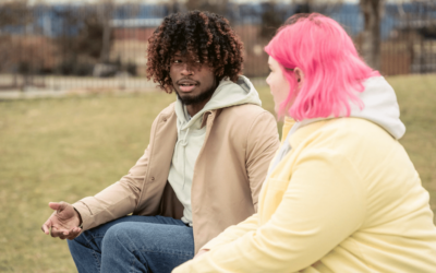man with afro textured hair talking to a woman with pink hair on a field