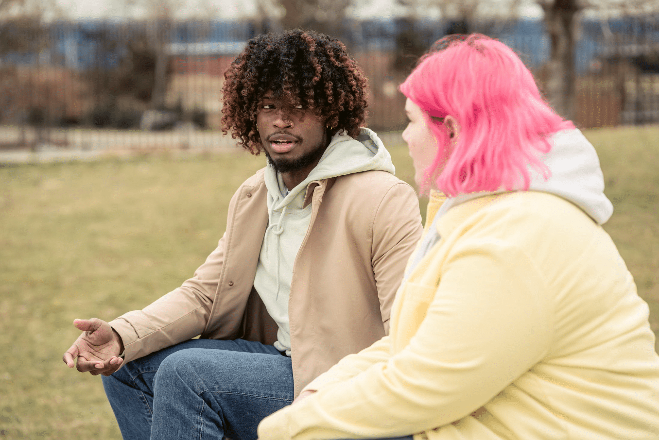 man with afro textured hair talking to a woman with pink hair on a field