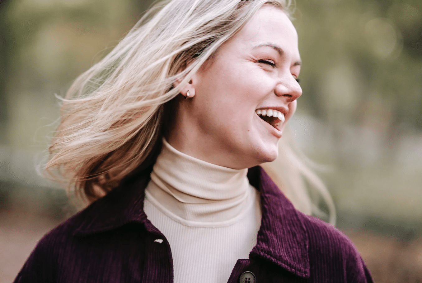 blonde woman in a cream roll neck looking to her right laughing