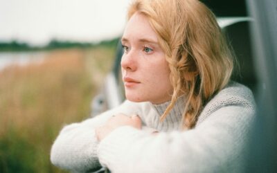 strawberry blonde lady wearing a white jumper looking outside a car window
