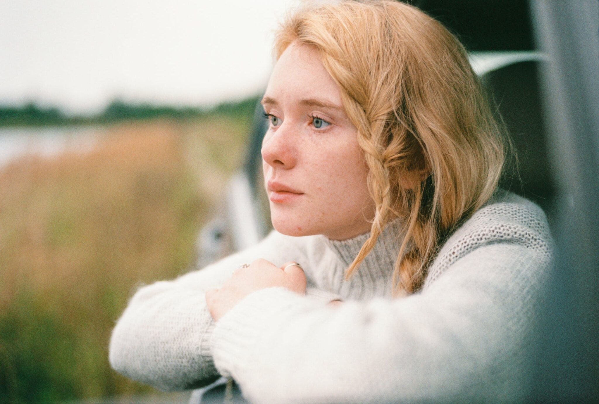 strawberry blonde lady wearing a white jumper looking outside a car window