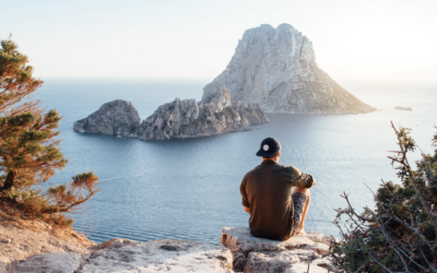 man wearing a cap sitting on a rock overlooking the sea