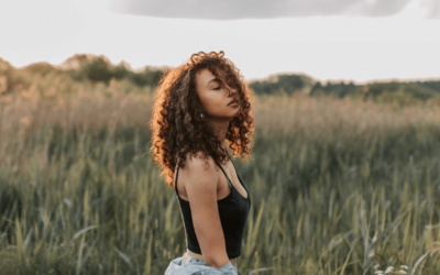 a woman with afro textured hair in a field with the sun setting behind her