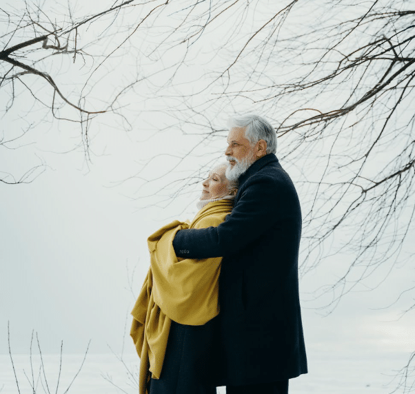 white older couple embracing each other with a grey sky in the background