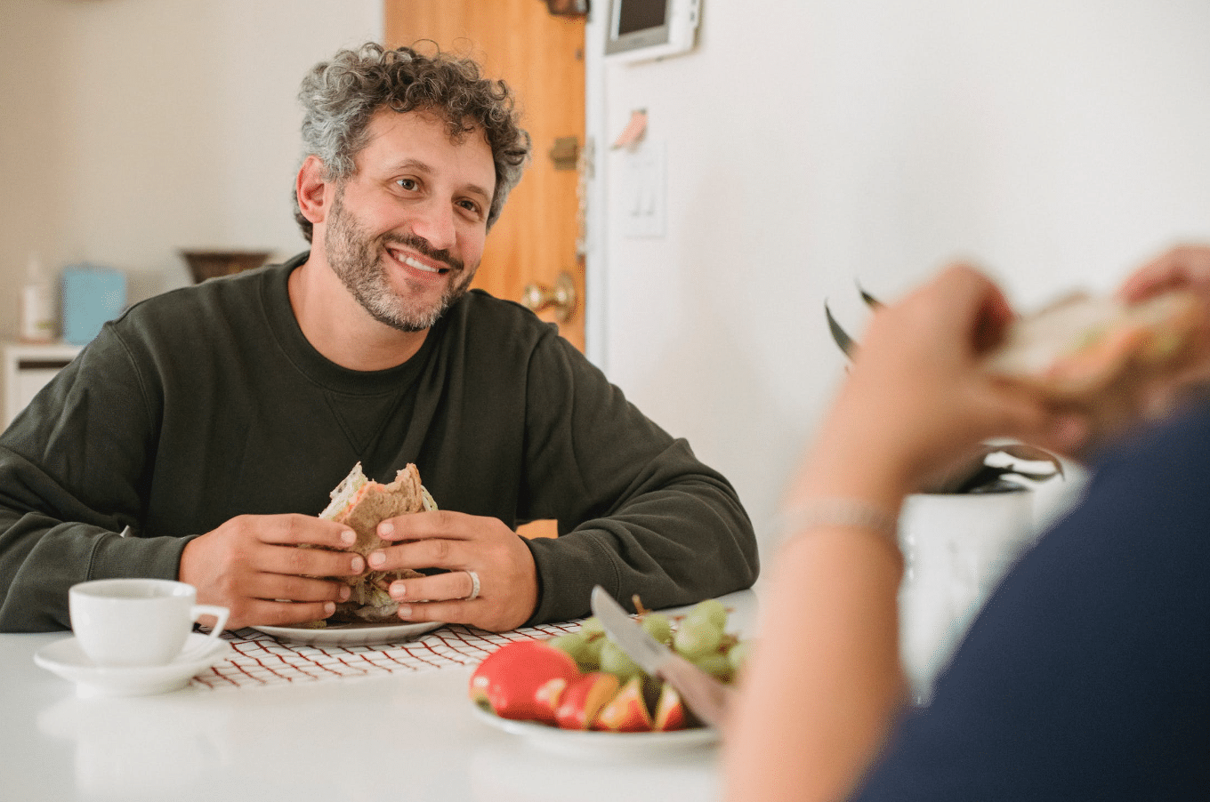 man smiling and eating his sandwich at the table
