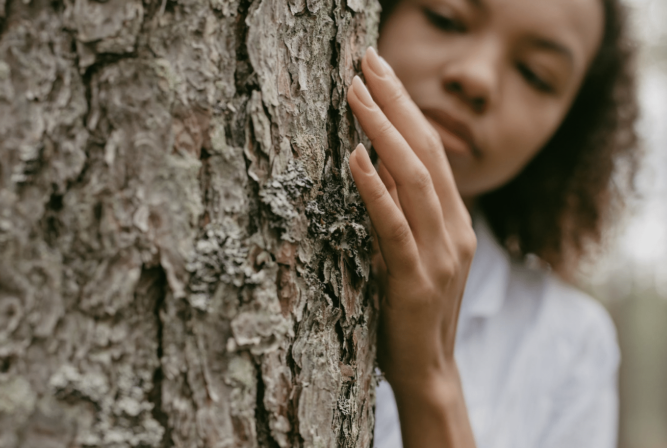 woman by a tree with her hand touching the bark