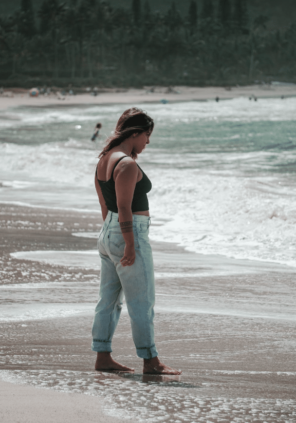 young woman wearing jeans on the beach looking down to the water