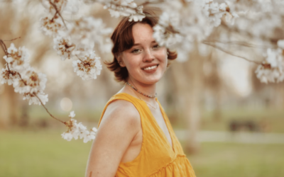 young woman by a blossom tree smiling wearing a yellow sleeveless top