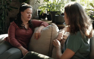two burnette women talking on a sofa, one with downs syndrome