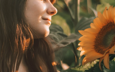 brunette lady with a fringe smiling and looking to sunflowers in a field