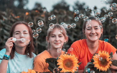three teenager females blowing bubbles and sitting behind sunflowers in a field