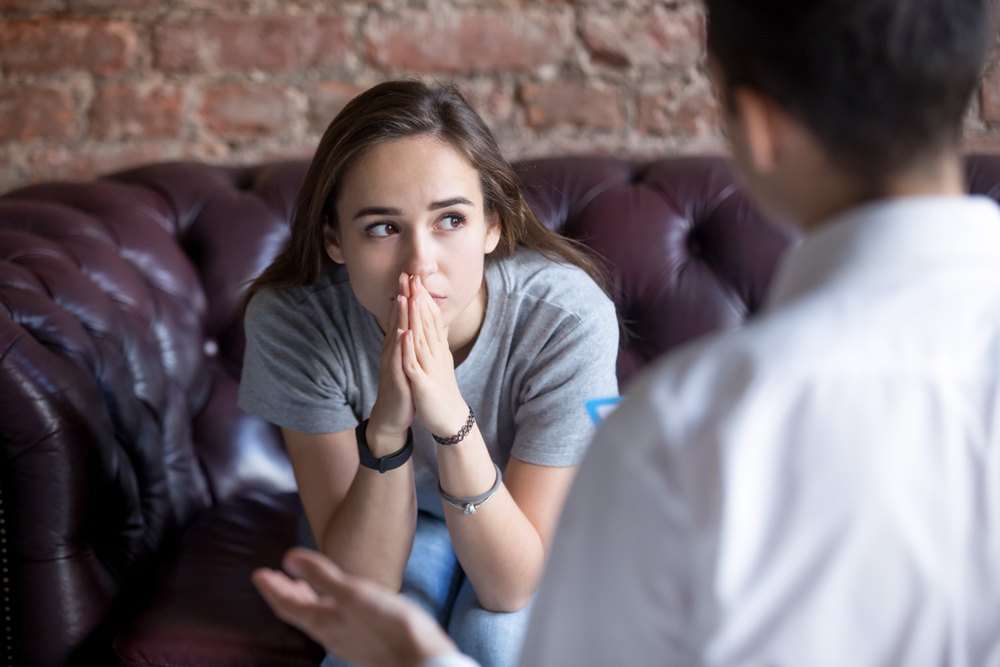 A young woman is looking anxious across from a professional therapist, depicting the signs of eating disorder in teenager. 
