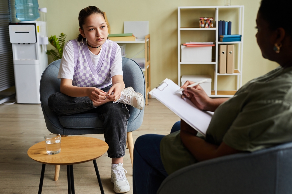 A female teen sitting in comfy chair across from a professional counsellor, showing there is help available for teenage eating disorders. 
